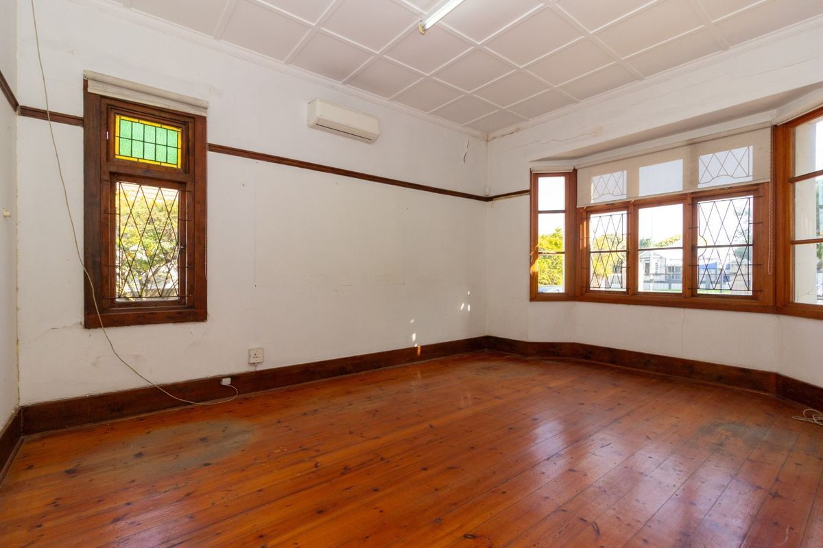 An empty office space featuring original timber flooring, a bay window with stained glass accents, and a coffered ceiling.