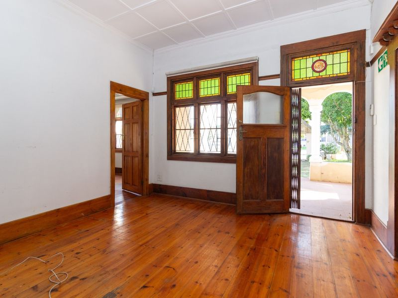 An empty office space featuring original hardwood flooring, timber door frames, and charming stained glass windows, offering direct access to an outdoor area.