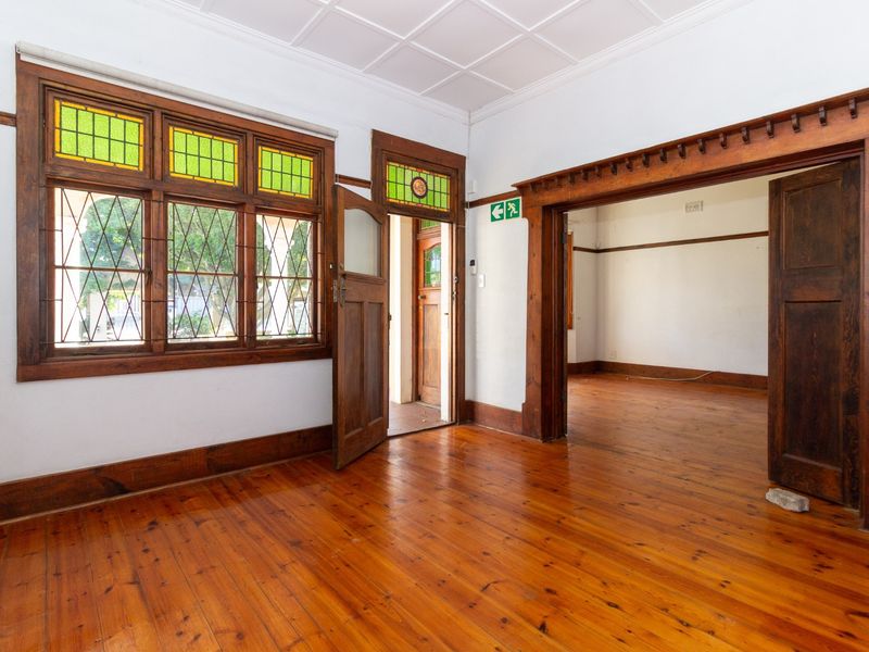 An empty office space featuring original timber flooring, ornate timber door frames, and stained glass window detailing, offering a classic professional aesthetic.
