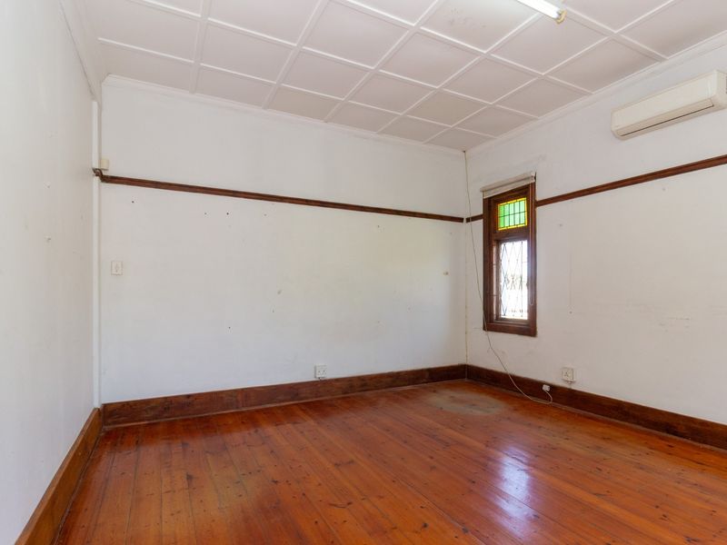 An empty office space featuring polished timber flooring, a stained glass window, and a wall-mounted split system air conditioner.