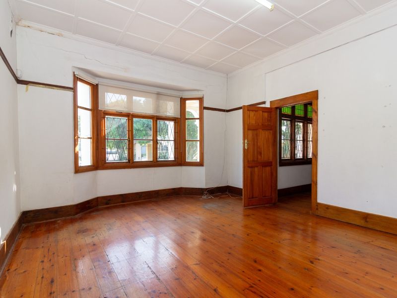 An empty office space featuring original timber flooring, a bay window with leaded glass details, and classic timber door frames.
