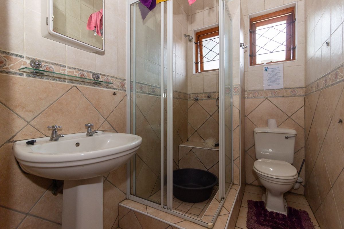 A functional bathroom featuring a pedestal basin, a glass-enclosed shower, and a toilet, finished with neutral wall and floor tiling.