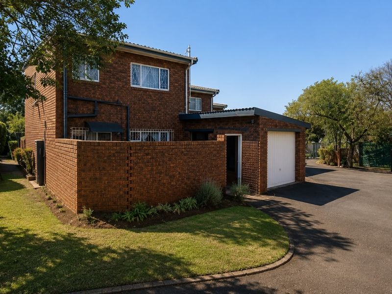 Front exterior view of a face brick townhouse featuring a single garage, paved driveway, and established garden area within a secure complex.