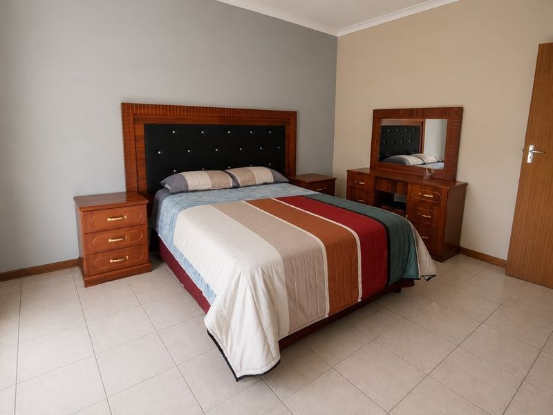 A well-maintained bedroom featuring neutral wall tones, tiled flooring, and classic cornice detailing, offering a clean and functional living space.