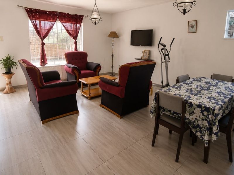 Open-plan living and dining area featuring neutral tiled flooring, large windows with security bars, and direct access to the exterior.