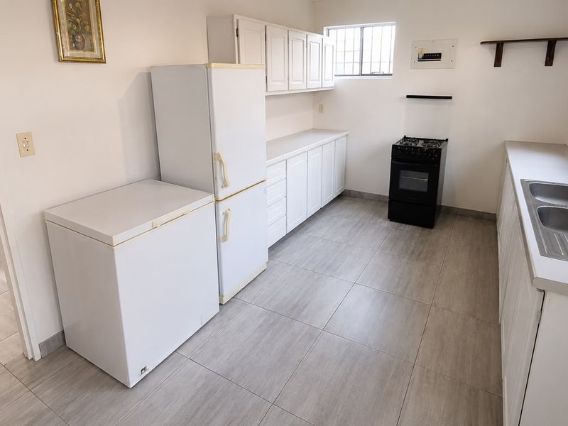 A functional kitchen featuring white cabinetry, tiled flooring, a double stainless steel sink, and a freestanding stove.