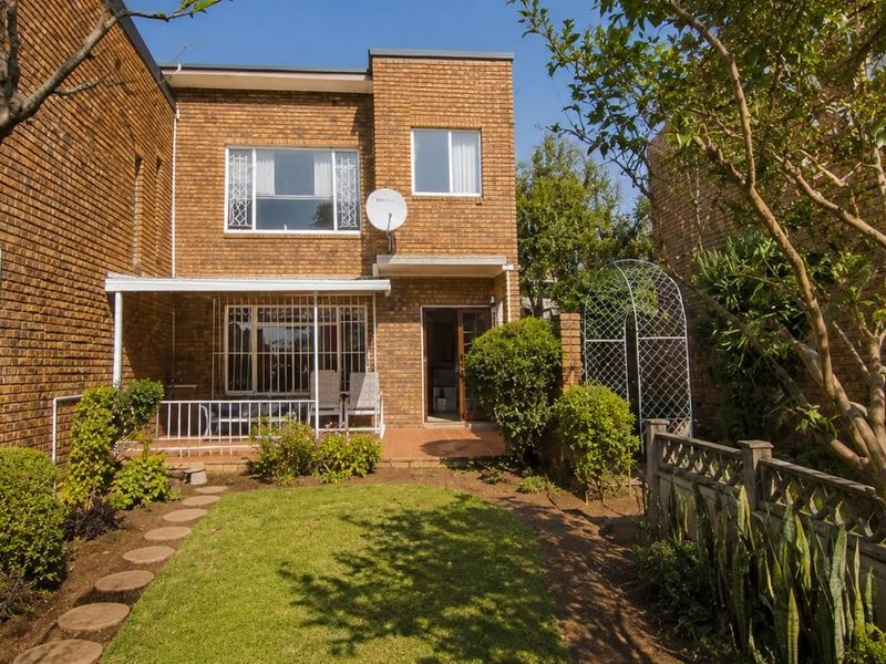 Rear view of a brick townhouse featuring a private garden, paved patio area, and established landscaping.