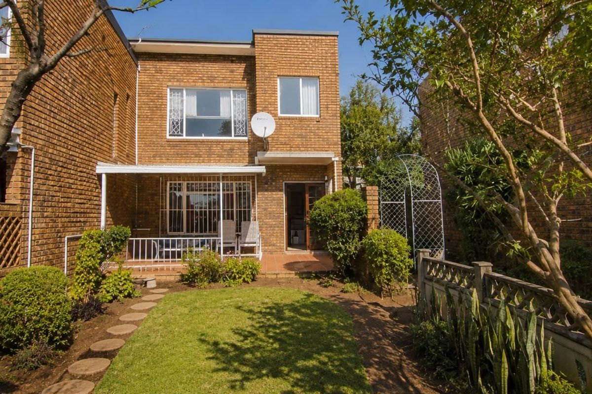Rear view of a brick townhouse featuring a private garden, paved patio area, and established landscaping.