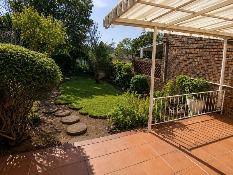 A private rear garden featuring a tiled patio with a covered roof, brick boundary walls, and a landscaped lawn area with stepping stones.
