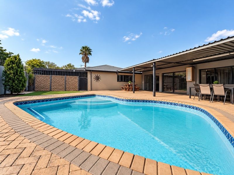 A well-maintained outdoor entertainment area featuring a swimming pool with paved surround and a spacious covered patio area.