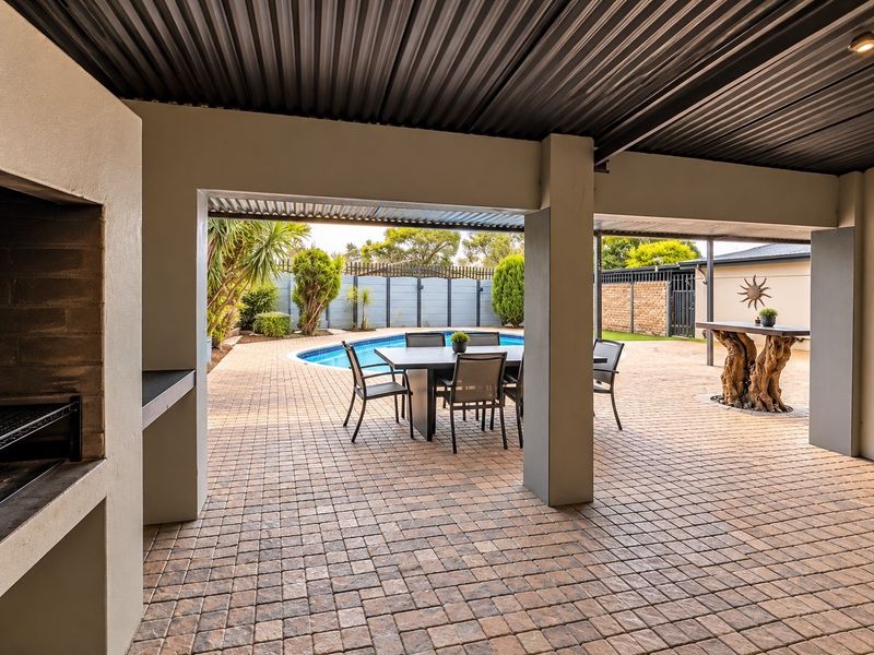 Covered outdoor patio featuring a built-in braai, paved flooring, and direct access to the swimming pool and garden area.