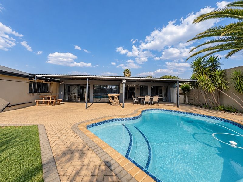 Spacious outdoor entertainment area featuring a paved patio, covered veranda, and a well-maintained swimming pool, perfect for outdoor living and relaxation.