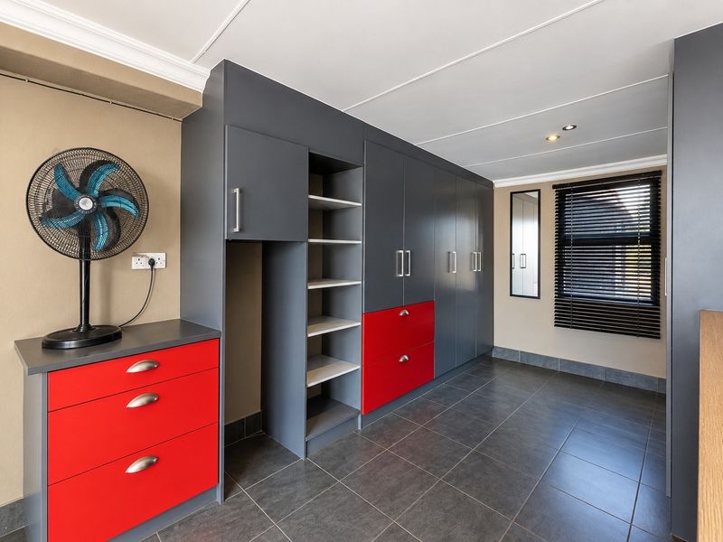 A clean bedroom featuring modern built-in cupboards with a grey and red finish, dark floor tiles, and venetian blinds.