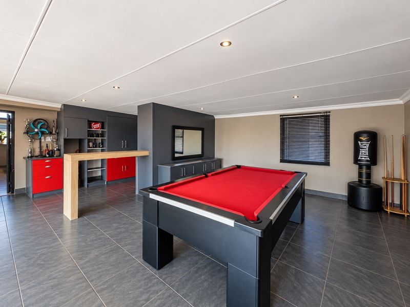 A modern entertainment room featuring a built-in bar area with cabinetry, tiled flooring, and recessed lighting, ideal for a home lounge or games room.
