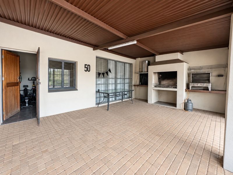 Covered outdoor patio featuring paved flooring and a built-in braai area, providing a functional space for outdoor entertaining.