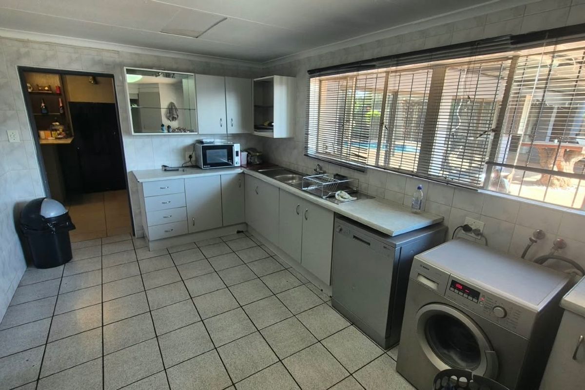 A functional kitchen featuring tiled walls and flooring, ample built-in cabinetry, and a large window providing natural light and views of the outdoor area.