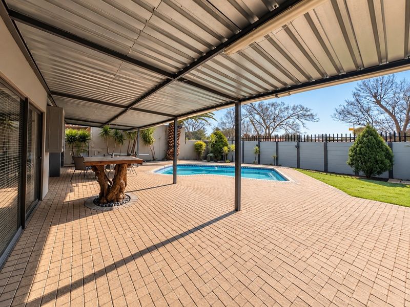 Spacious outdoor entertainment area featuring a covered patio with paved flooring, overlooking a private swimming pool and landscaped garden.