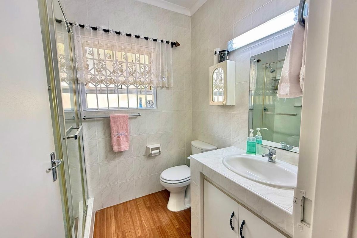 A functional bathroom featuring a vanity with basin, toilet, and a glass-enclosed shower, finished with tiled walls and wood-look flooring.