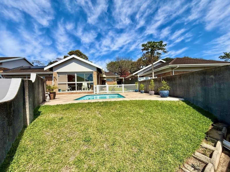Rear exterior view of the townhouse featuring a private swimming pool, paved patio area, and a well-maintained lawn enclosed by boundary walls.