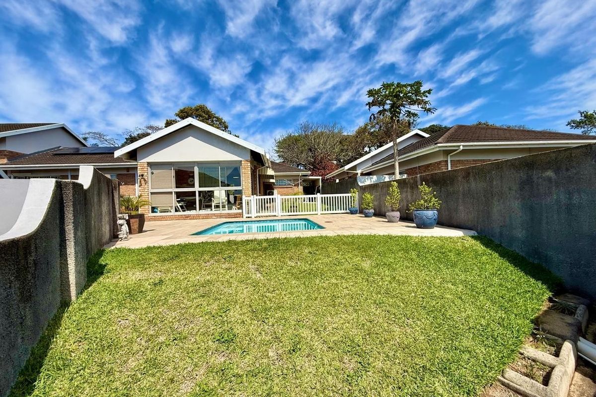 Rear exterior view of the townhouse featuring a private swimming pool, paved patio area, and a well-maintained lawn enclosed by boundary walls.