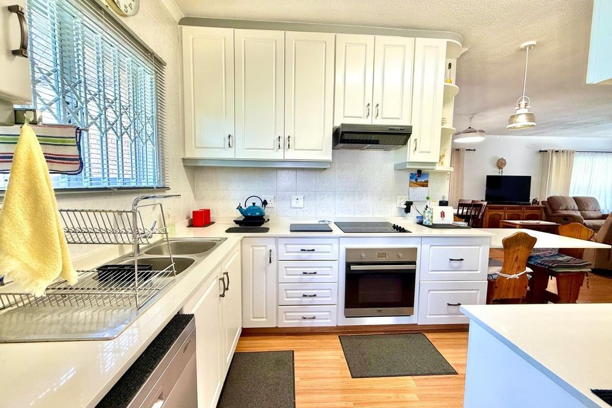 A functional kitchen featuring white cabinetry, built-in oven, electric hob, extractor fan, and a double basin sink with a tiled backsplash.