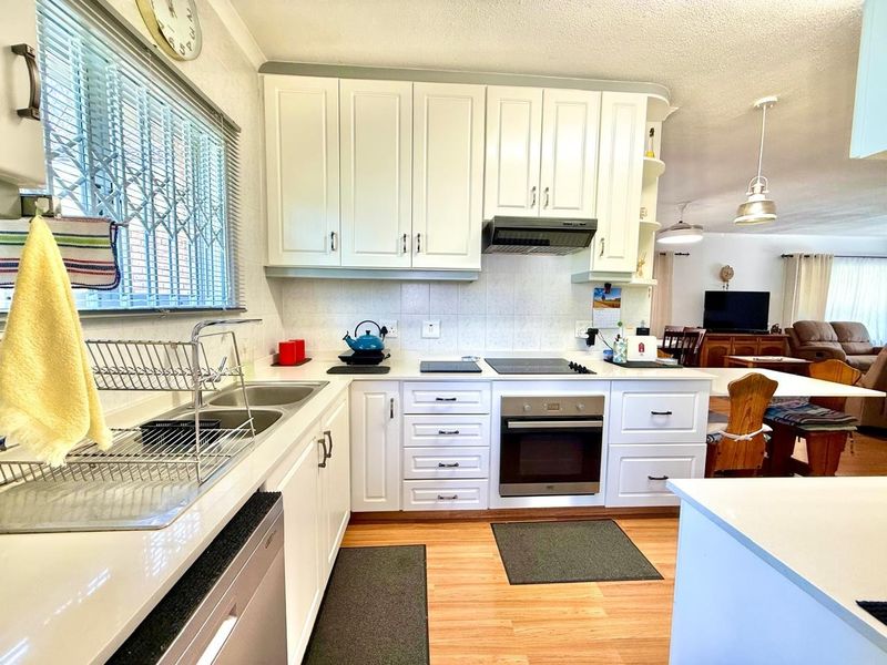 A functional kitchen featuring white cabinetry, built-in oven, electric hob, extractor fan, and a double basin sink with a tiled backsplash.