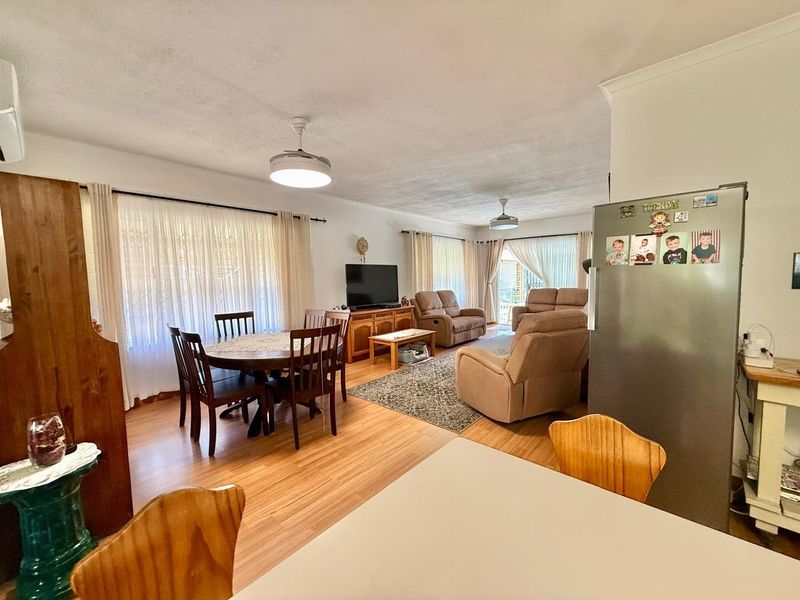 Spacious open-plan living and dining area featuring laminate flooring, ceiling fans, and large windows providing natural light.