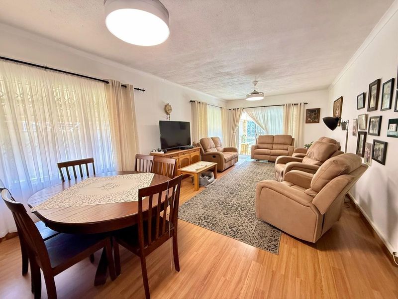 Spacious open-plan living and dining area featuring laminate flooring, ceiling fans, and large windows providing natural light with access to the patio.