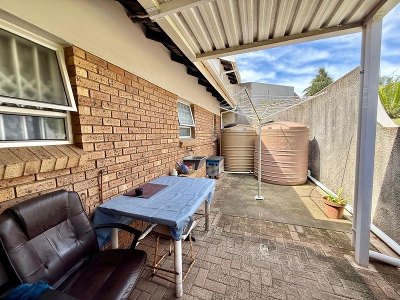 A covered outdoor patio area featuring brick walling, concrete paving, and installed water storage tanks, providing a functional utility space.
