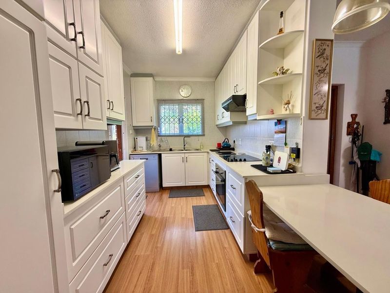 A functional kitchen featuring white cabinetry, laminate flooring, built-in oven, electric cooktop, and a breakfast counter, offering a clean and practical workspace.