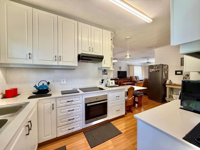 Open plan kitchen featuring white cabinetry, integrated appliances, and laminate flooring, flowing seamlessly into the adjacent living and dining area.