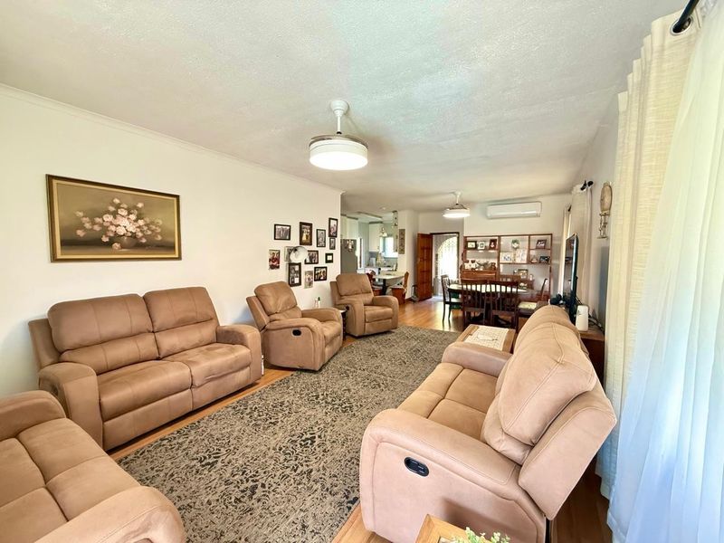 Spacious open-plan living and dining area featuring laminate flooring, ceiling fans, and a wall-mounted air conditioning unit.