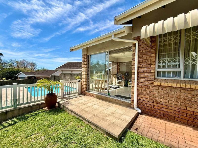 Rear exterior view of the townhouse featuring a paved patio, brick facade, sliding door access, and a private swimming pool area.
