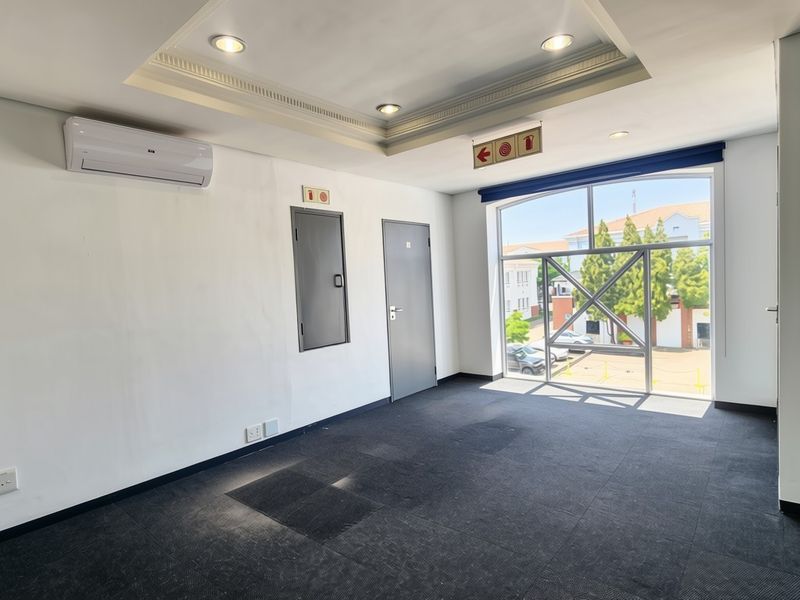 A bright, empty office space featuring recessed ceiling lighting, a split-system air conditioner, and large windows providing natural light and exterior views.