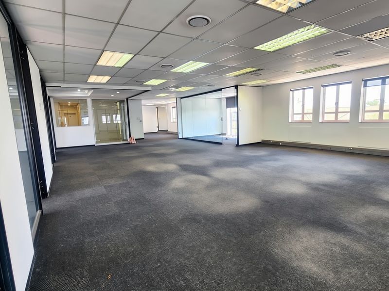 A spacious, open-plan office area featuring modern glass partitioning, suspended ceilings with recessed lighting, and durable carpet tiles throughout.