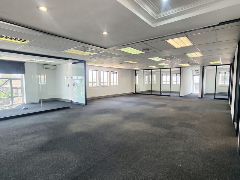 Spacious open-plan office area featuring glass partitioning, suspended ceilings with recessed lighting, and carpeted flooring, offering a clean and professional workspace.