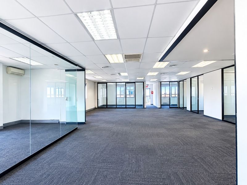 Spacious open-plan office area featuring modern glass partitioning, suspended ceilings with recessed lighting, and durable carpet tiles throughout.