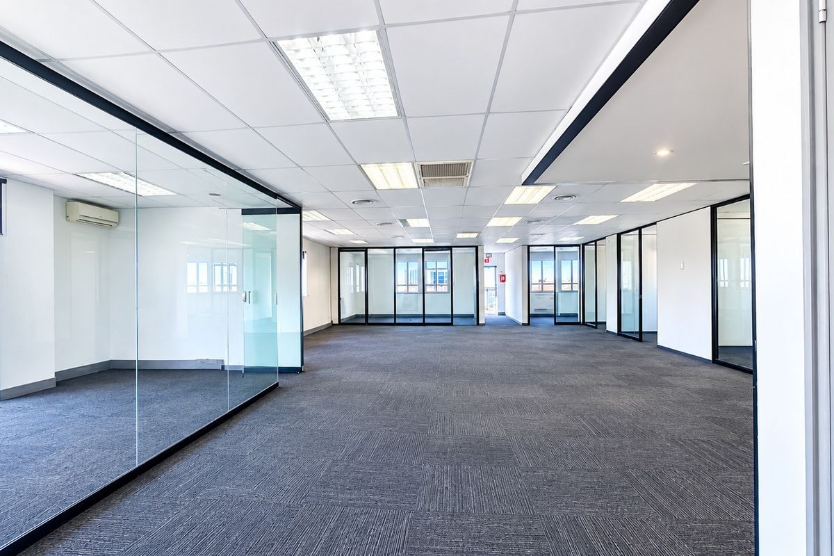 Spacious open-plan office area featuring modern glass partitioning, suspended ceilings with recessed lighting, and durable carpet tiles throughout.
