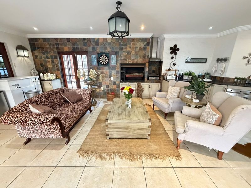 Spacious open-plan living area featuring a built-in braai, stone feature wall, tiled flooring, and integrated cabinetry, perfect for relaxed indoor entertaining.