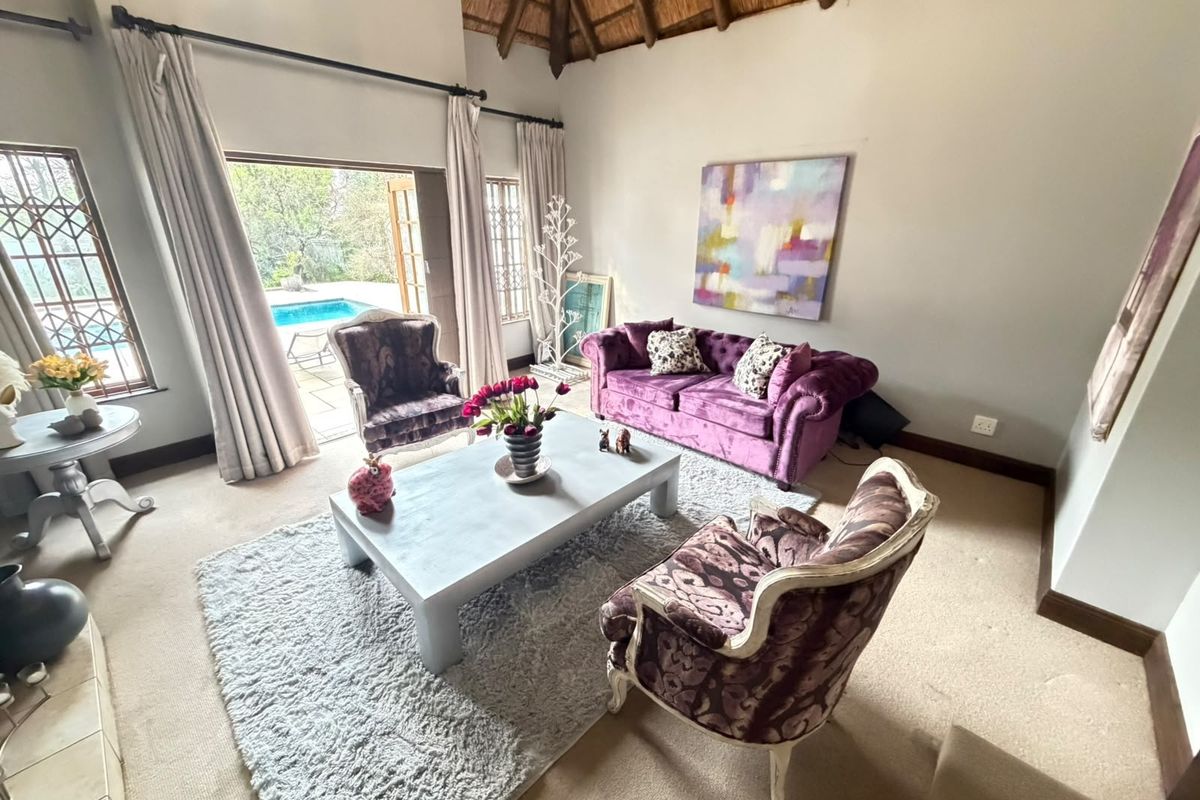 A spacious living room featuring a high vaulted thatched ceiling with exposed timber rafters and sliding doors leading to an outdoor pool area.