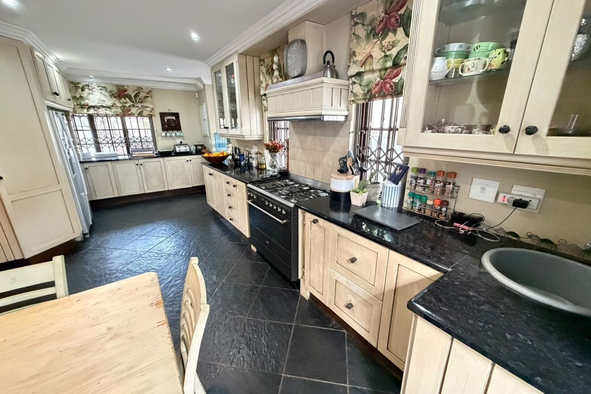 Spacious kitchen featuring cream cabinetry, dark granite countertops, a gas stove with extractor fan, and dark tiled flooring.