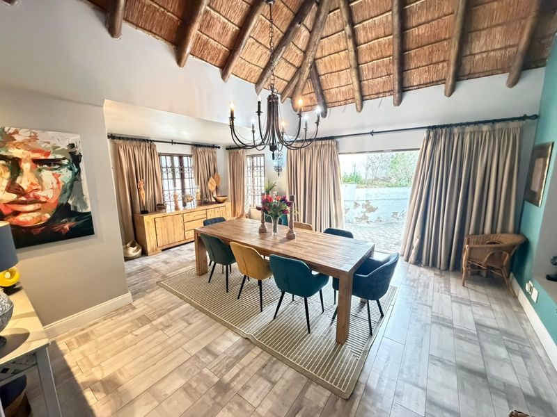 Spacious dining room featuring a high vaulted thatched ceiling with exposed timber rafters, tiled flooring, and large sliding doors leading to the patio.