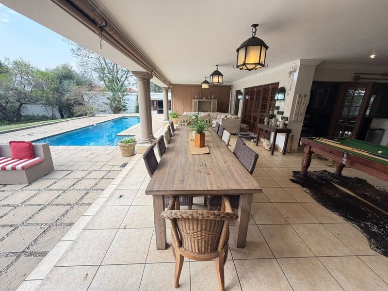 Spacious covered patio featuring tiled flooring, stone columns, and direct access to a swimming pool, ideal for outdoor entertaining.