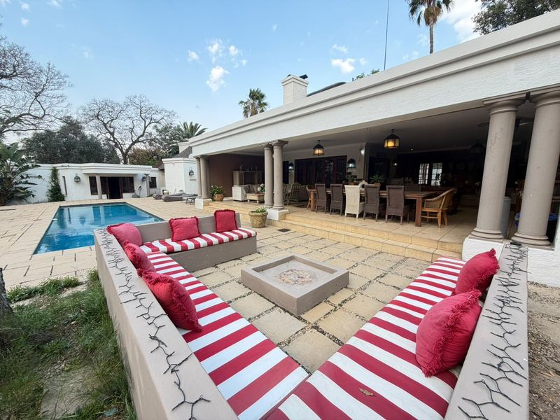 Spacious covered patio featuring a built-in fire pit, integrated seating, and direct access to a swimming pool, ideal for outdoor entertaining.