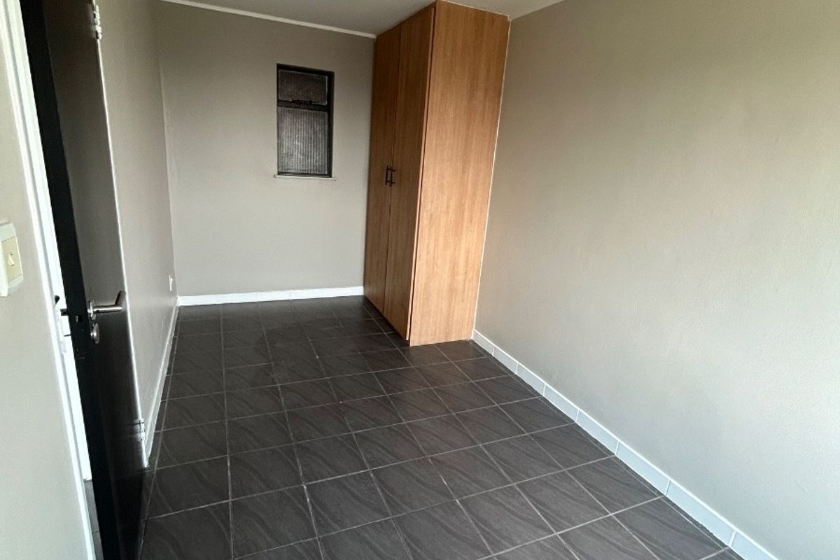 An empty bedroom featuring dark tiled flooring, neutral wall paint, and a built-in wooden wardrobe.