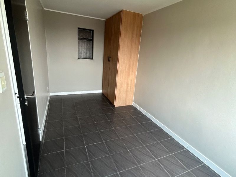 An empty bedroom featuring dark tiled flooring, neutral wall paint, and a built-in wooden wardrobe.