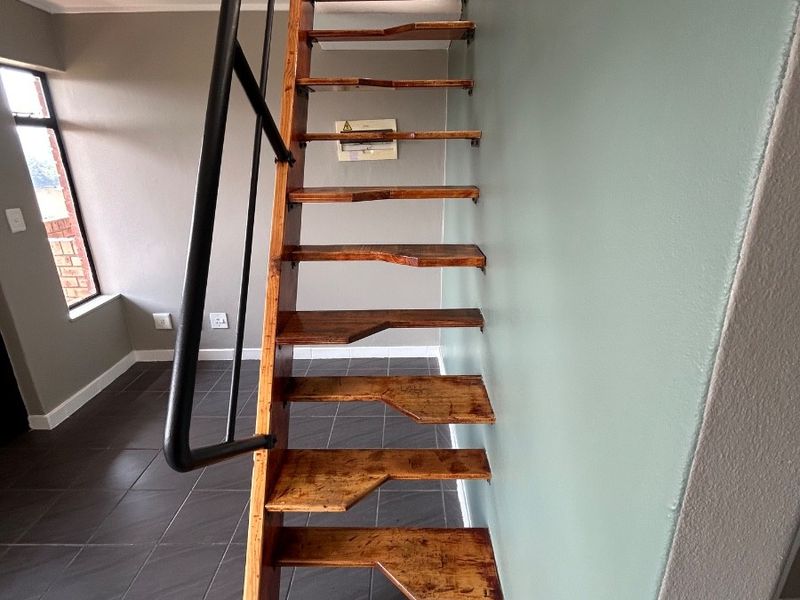 An open-plan living area featuring a steep wooden staircase with a metal handrail and dark tiled flooring.