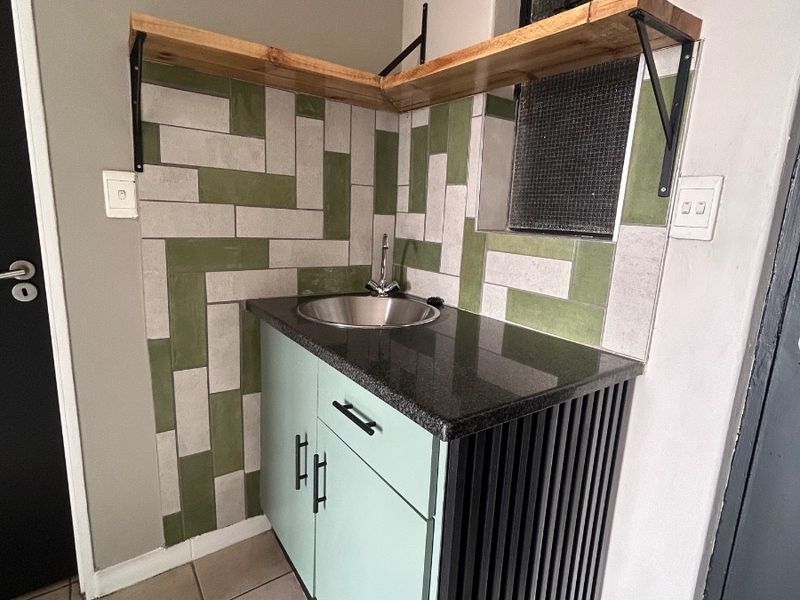 A compact scullery or prep area featuring custom cabinetry, a stone countertop, stainless steel sink, and decorative tiled backsplash with floating shelving.