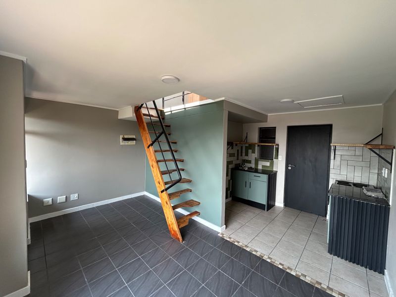 Open plan living area featuring a modern staircase, tiled flooring, and a compact kitchen corner with built-in cabinetry and shelving.