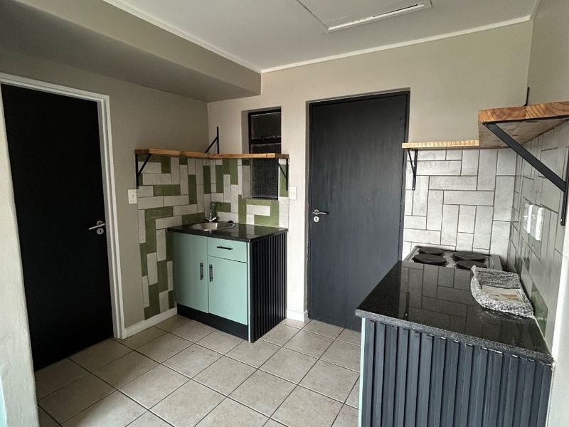 A compact, modern kitchen featuring built-in cabinetry, granite countertops, a tiled backsplash, and an electric hob, finished with neutral ceramic floor tiles.
